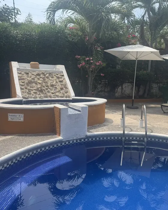 Pool with waterfall, sun loungers and umbrellas surrounded by a garden